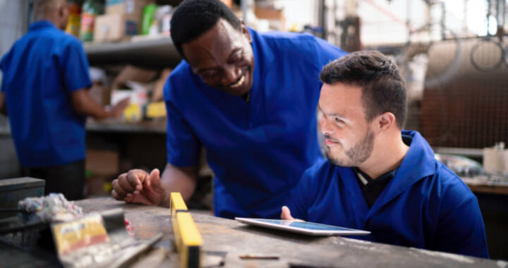 Person with a disability performing task on iPad while coworker smiles next to him